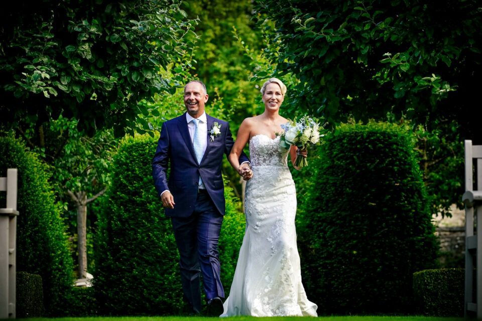 Bride and groom walk into the garden ceremony at a Temple Guiting Barns Wedding in Gloucestershire