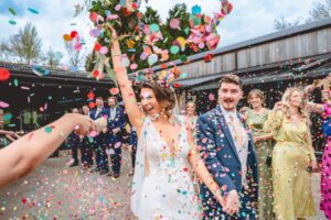 Bride laughing raising bouquet in a confetti storm at a wedding at Foxtail Barns wedding venue in Staffordshire.
