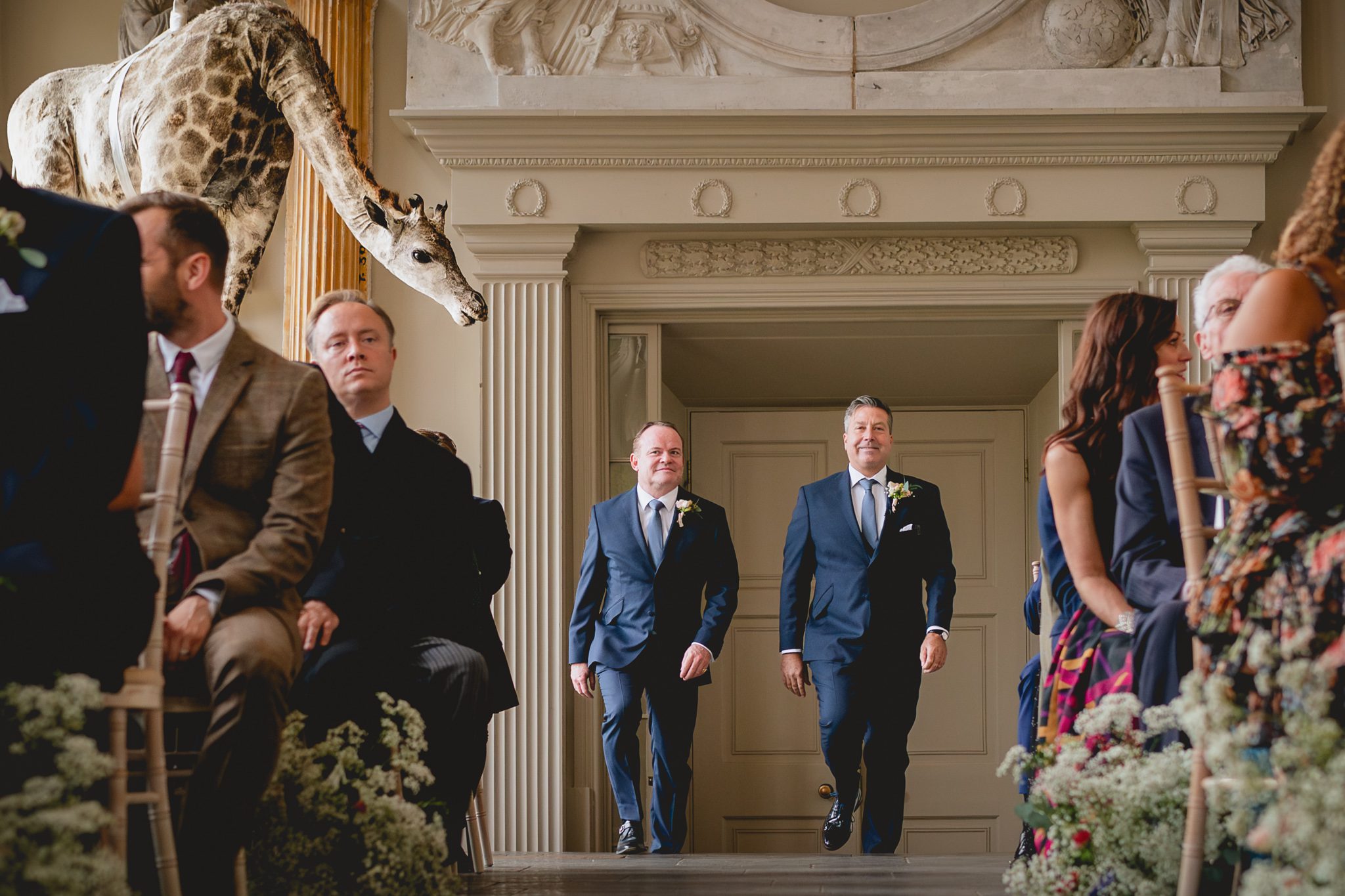Groom and Best Man walking down the aisle being watched by a giraffe