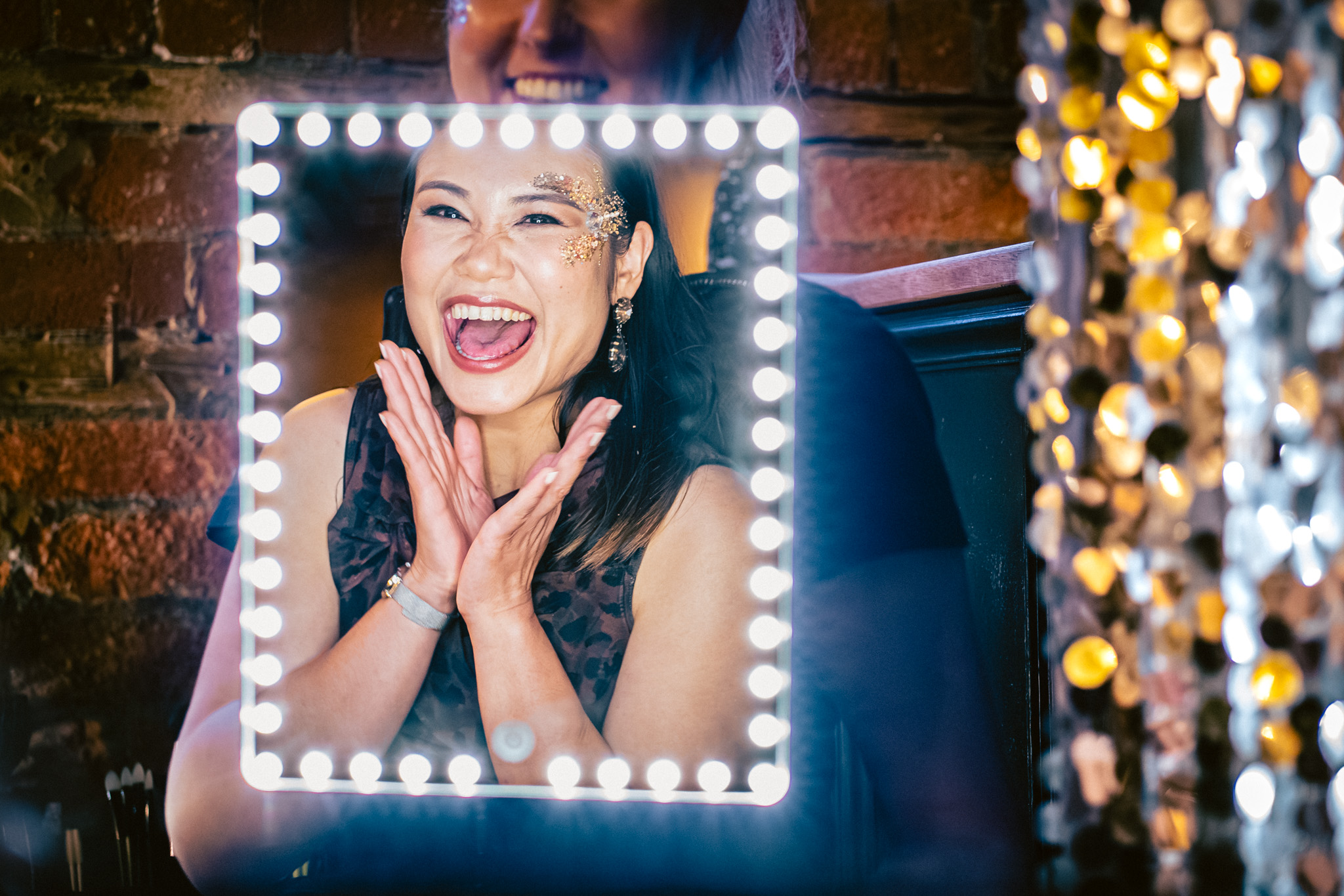 Smiling woman looking in a mirror having been glittered at a wedding reception at The Mowbray in Sheffield
