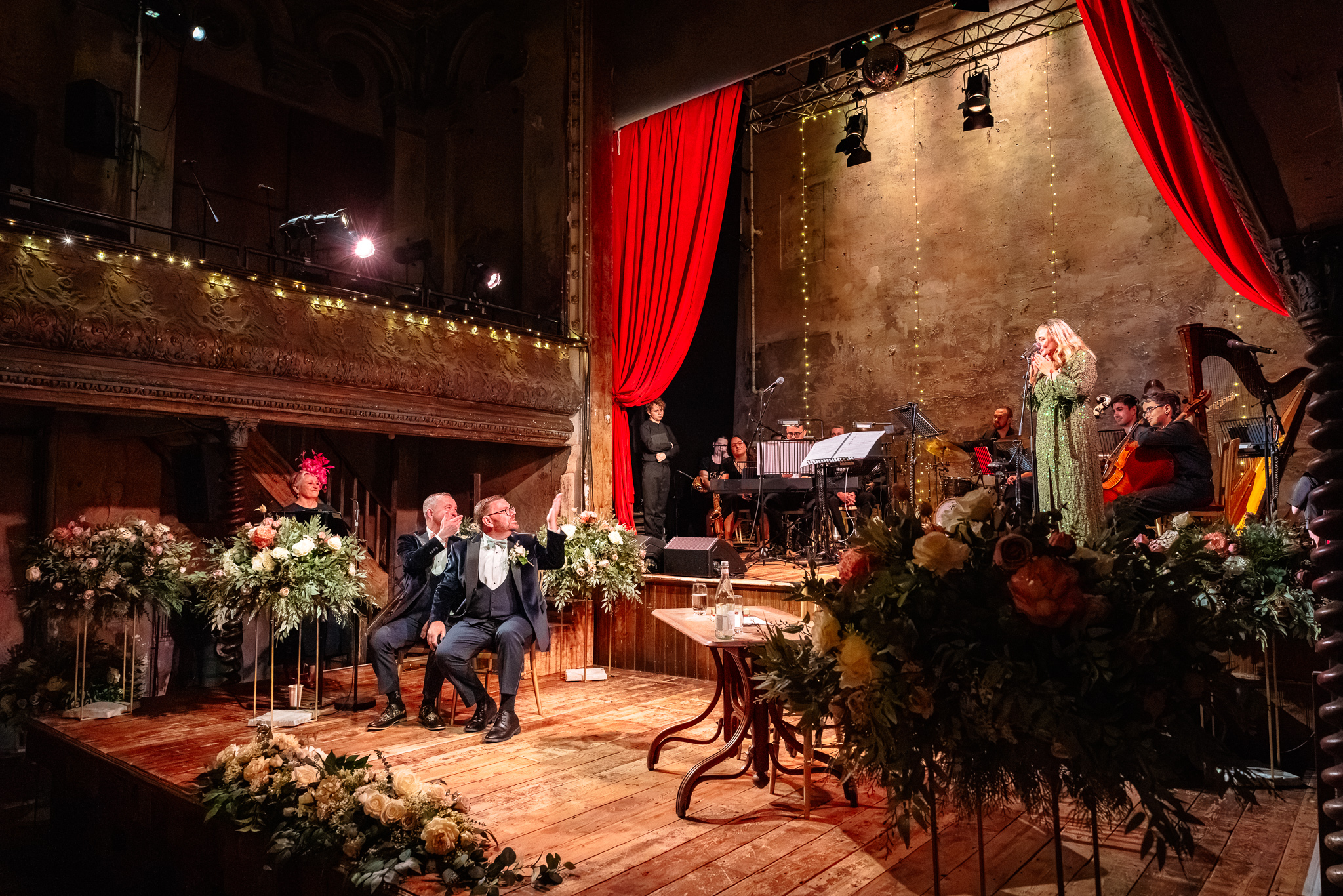 Same sex couple getting married at Wiltons Music Hall in London on a stage with a singer and orchestra